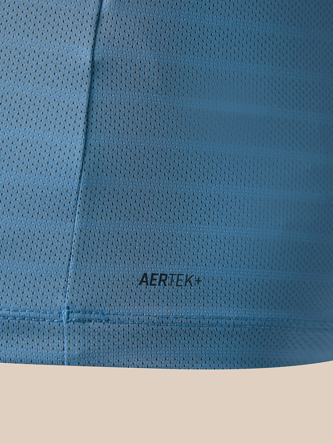 Close-up of a blue perforated athletic fabric with the AERTEK+ logo printed in black near the center, set against a light beige background.