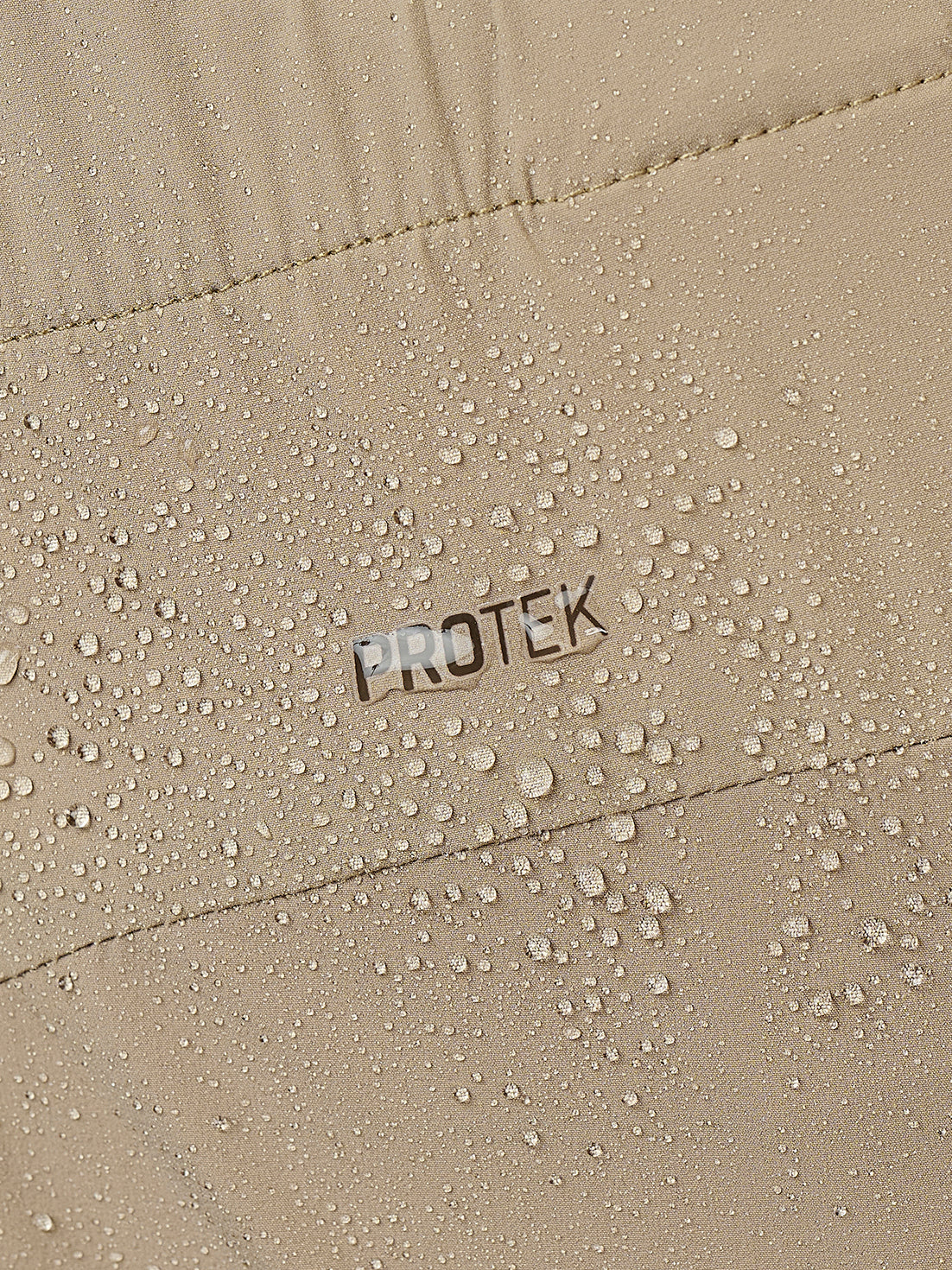 Close-up of a beige waterproof jacket or fabric with water droplets beading on the surface and the word PROTEK printed in the center.