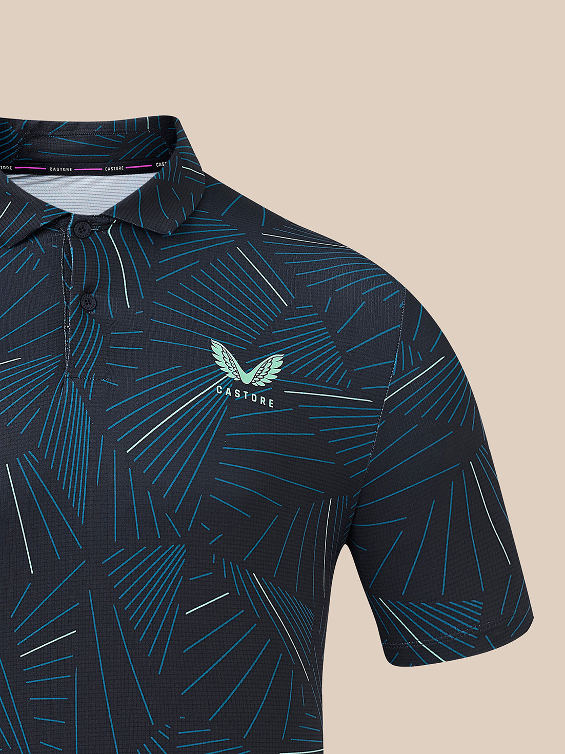 A close-up of a short-sleeve polo shirt with a dark navy base and an abstract geometric line pattern in teal, blue, and white. The chest features a teal winged logo with the text 'CASTORE.