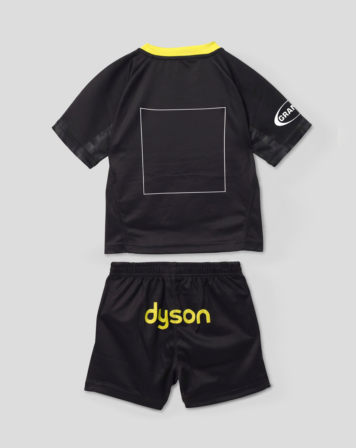 A toddler black short-sleeve jersey and matching shorts set from Dyson, shown flat-laid on a light gray background. The jersey features a bright yellow collar, a white outlined square on the back, and a white circular logo on the sleeve.