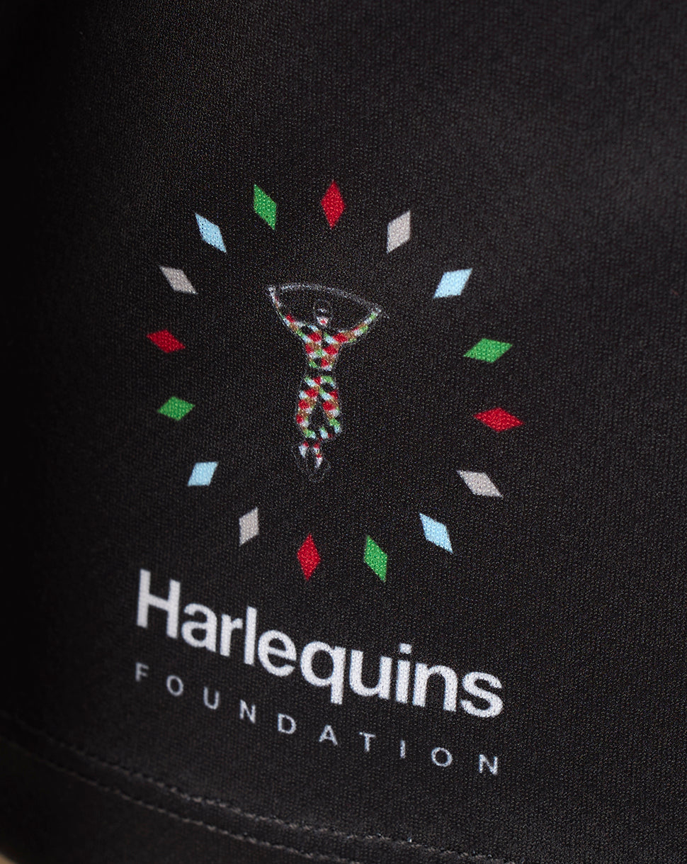 Close-up of a black fabric surface featuring a colorful embroidered or printed Harlequins Foundation logo with white text below.