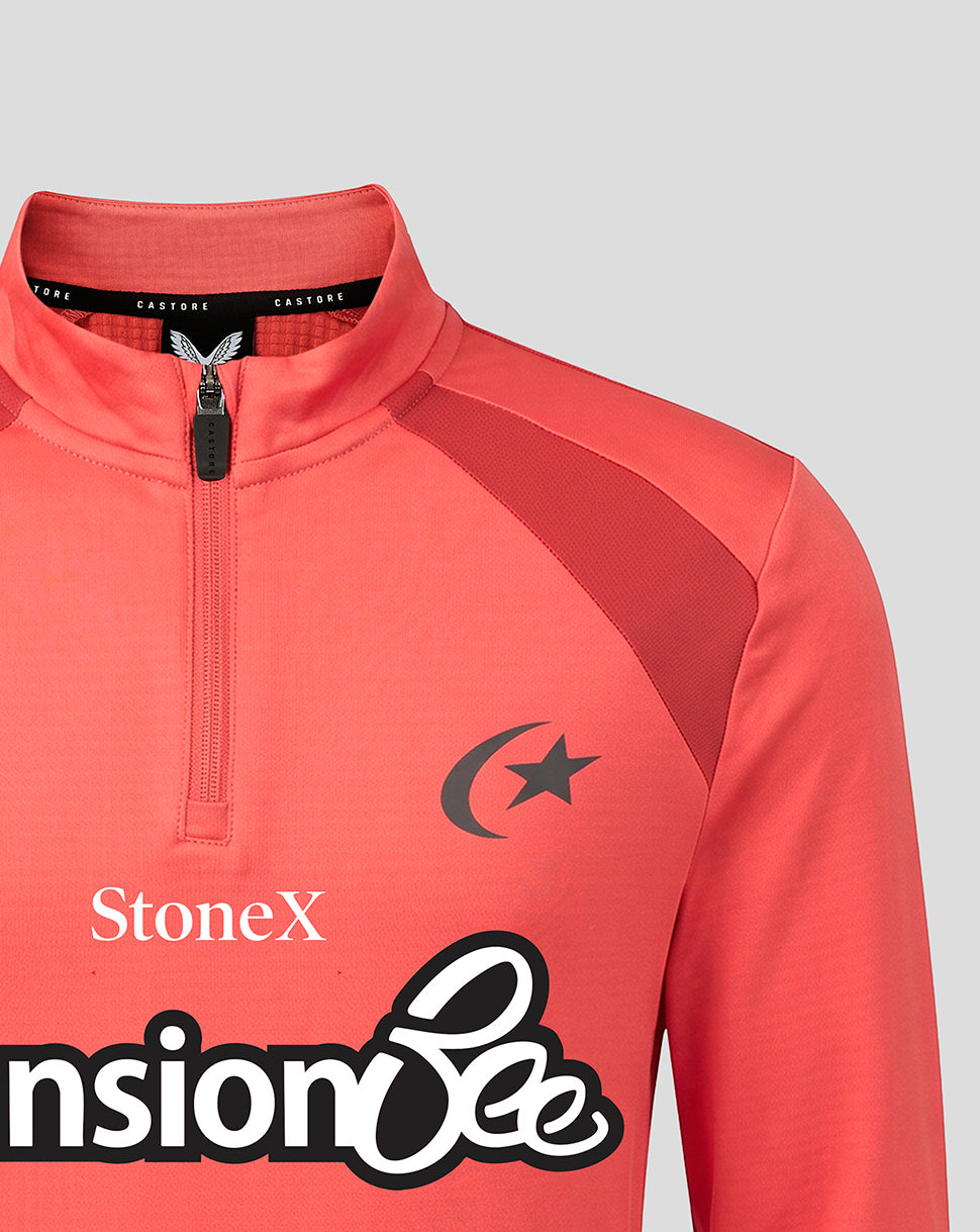 A close-up of a coral pink athletic quarter-zip pullover with dark red shoulder panels, featuring a black crescent and star logo on the chest and sponsor logos 'StoneX' and 'Pension Bee' printed on the front.