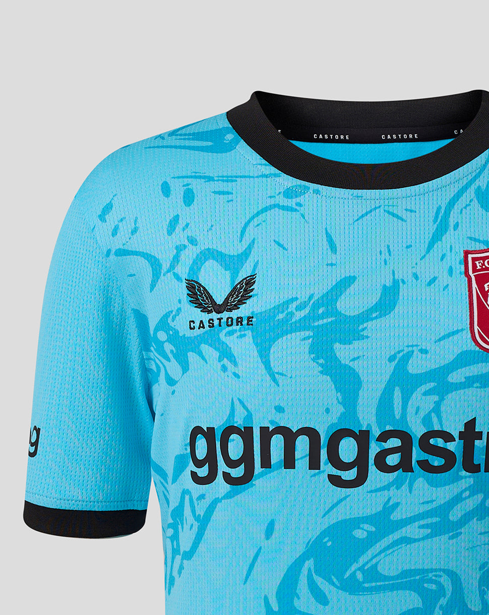Shoulder and chest close up of turquoise goalkeeper shirt showing crest on left chest, black collar edge, and blue graphic pattern.