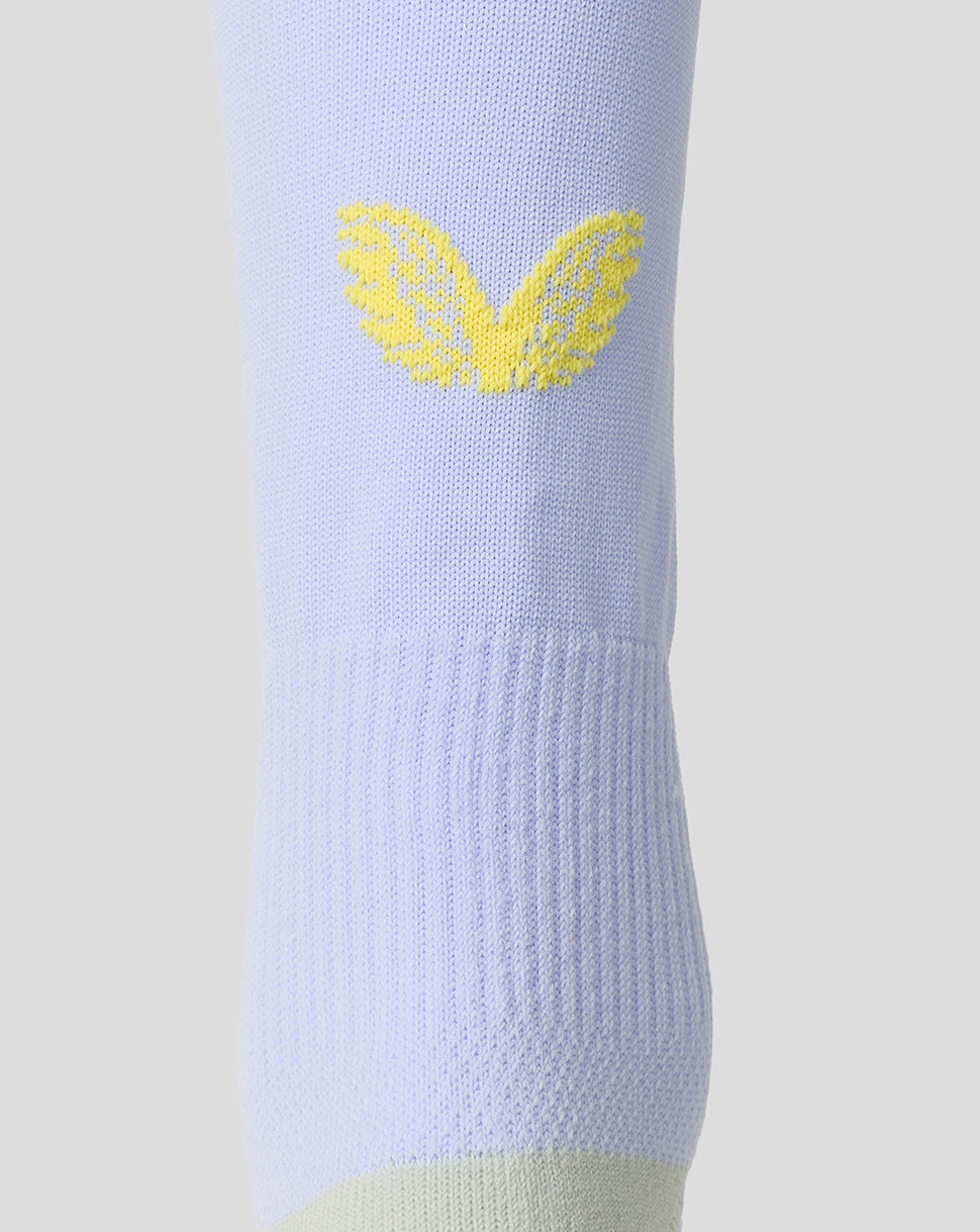 A close-up of a light periwinkle blue knit sock featuring a yellow embroidered wing logo on the upper calf, set against a solid light gray background.