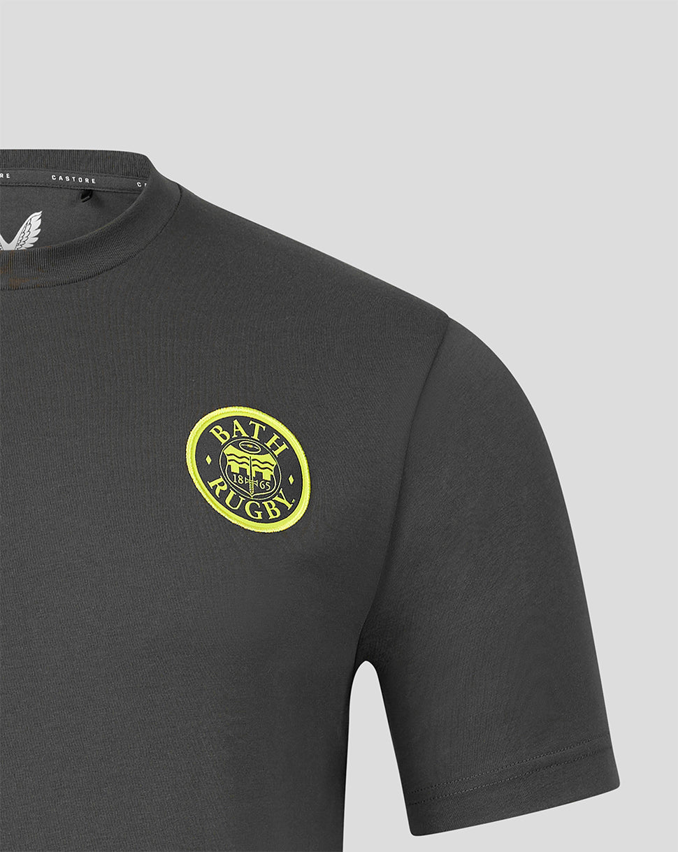 Close-up of a dark gray short-sleeve t-shirt featuring a circular yellow and black graphic on the left chest, set against a solid light gray background.