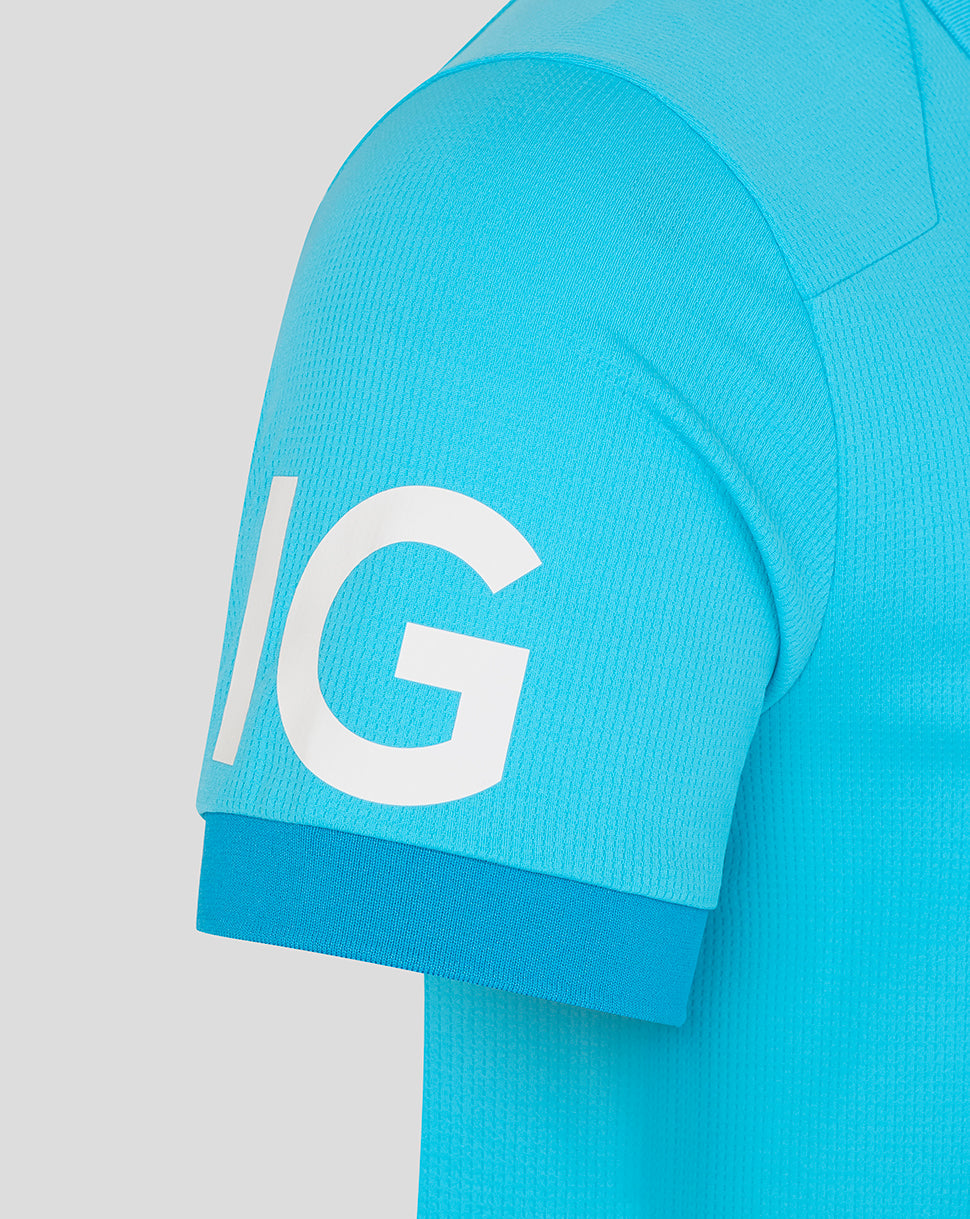 Close-up of a turquoise sports jersey with a large white letter 'IG' on the sleeve against a light gray background.