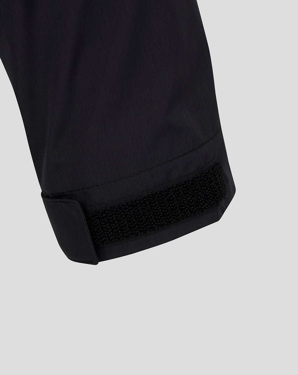 Close-up of a black garment cuff with a hook-and-loop fastening closure, shown against a light gray background.