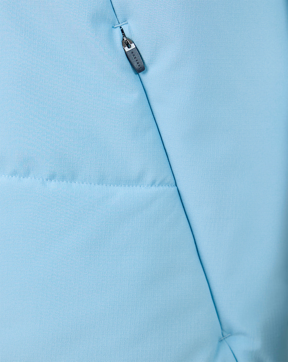 Close-up of light blue fabric showing a vertical zip pocket and diagonal seam on the training gilet.