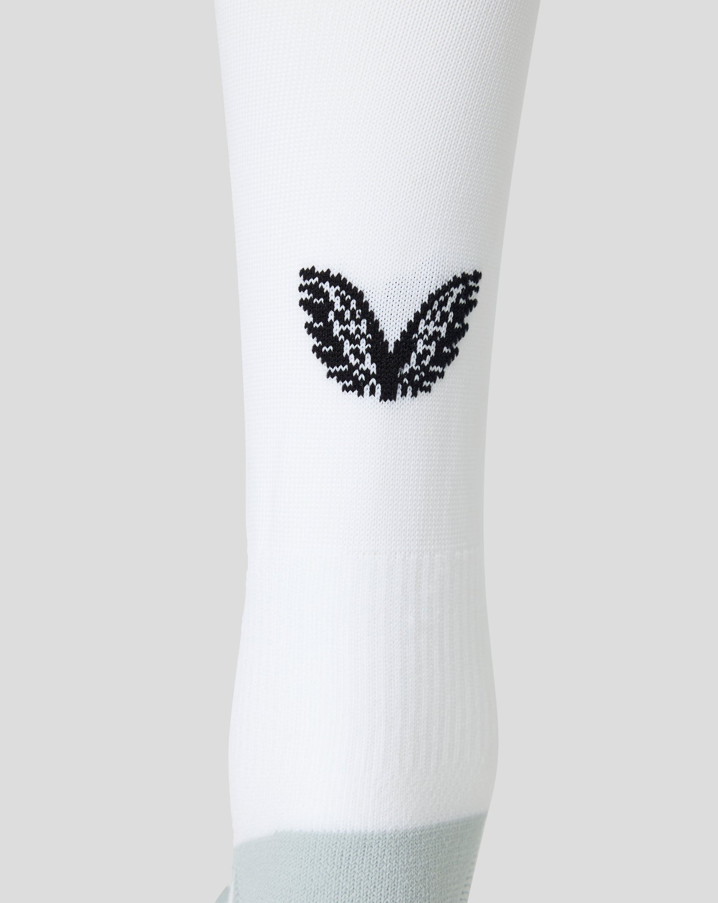 A close-up of a white athletic sock featuring a black knit wing design on the side and a light gray ribbed toe section, set against a solid light gray background.