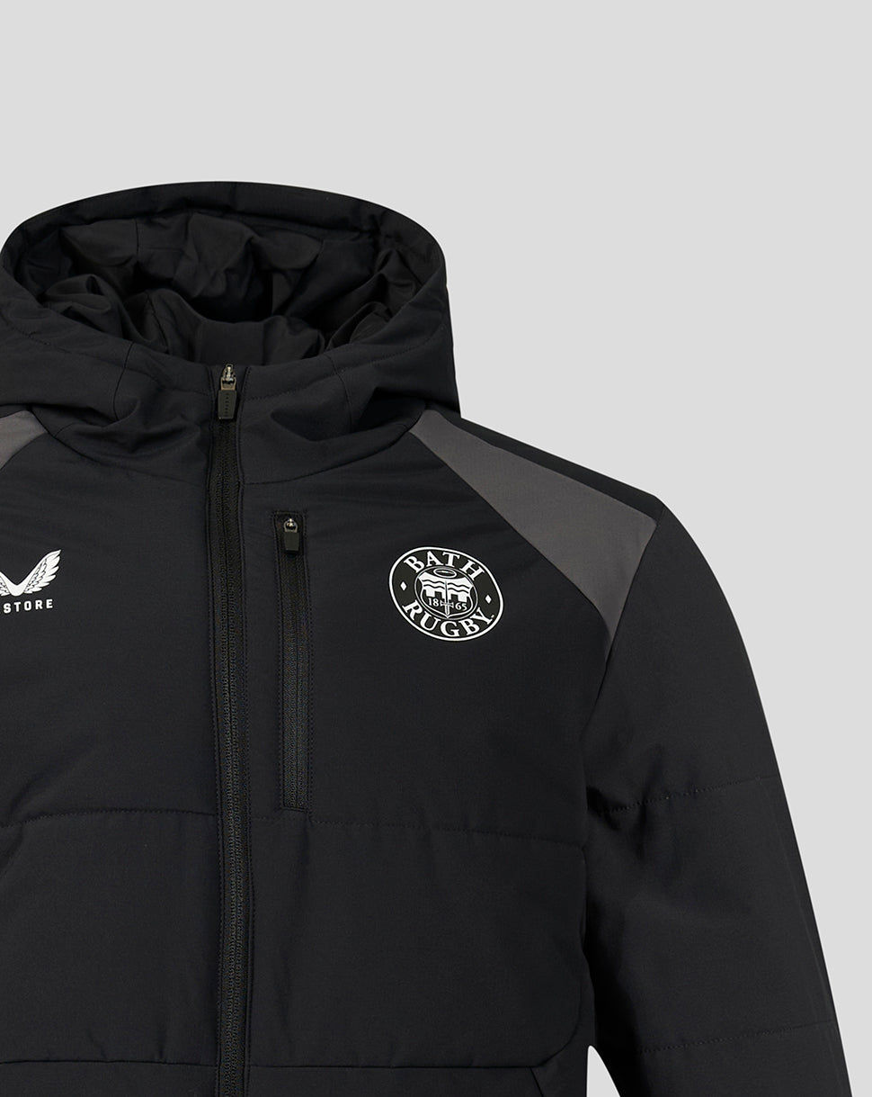 A close-up of a black hooded puffer jacket with a front zipper, featuring a circular 'BATH Rugby' logo on the left chest and a white winged logo on the right chest, set against a light gray background.