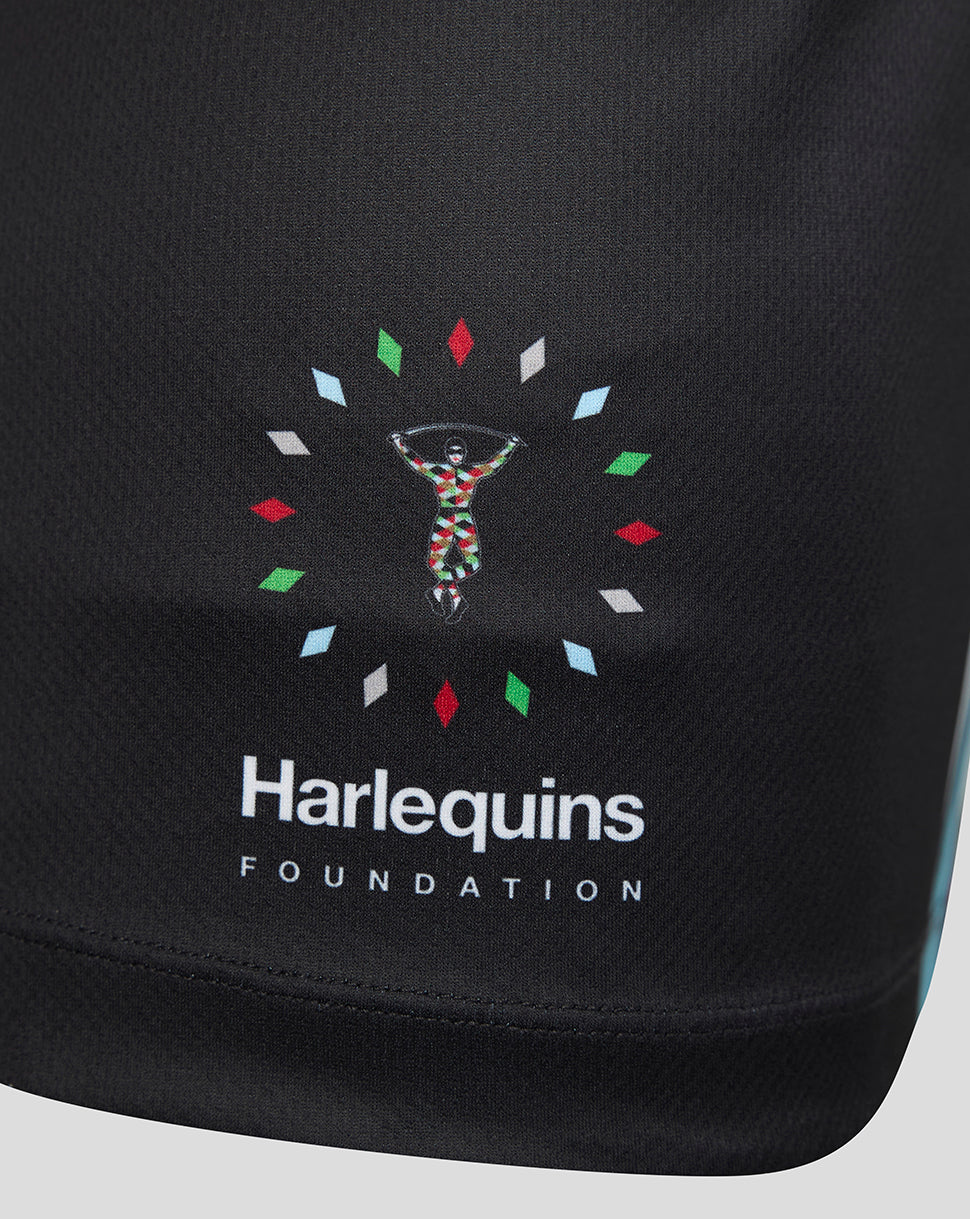 Close-up of a black athletic garment featuring the Harlequins Foundation logo printed on the front. The logo includes a colorful figure surrounded by small multicolored diamond shapes, with 'Harlequins' and 'FOUNDATION' in white text below.