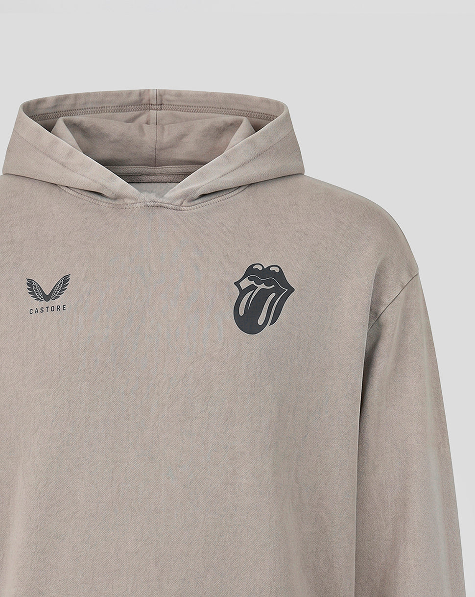 A close-up of a light taupe-beige hooded sweatshirt featuring a black Rolling Stones tongue-and-lips logo on the left chest and a black winged logo with 'CASTORE' text on the right chest.