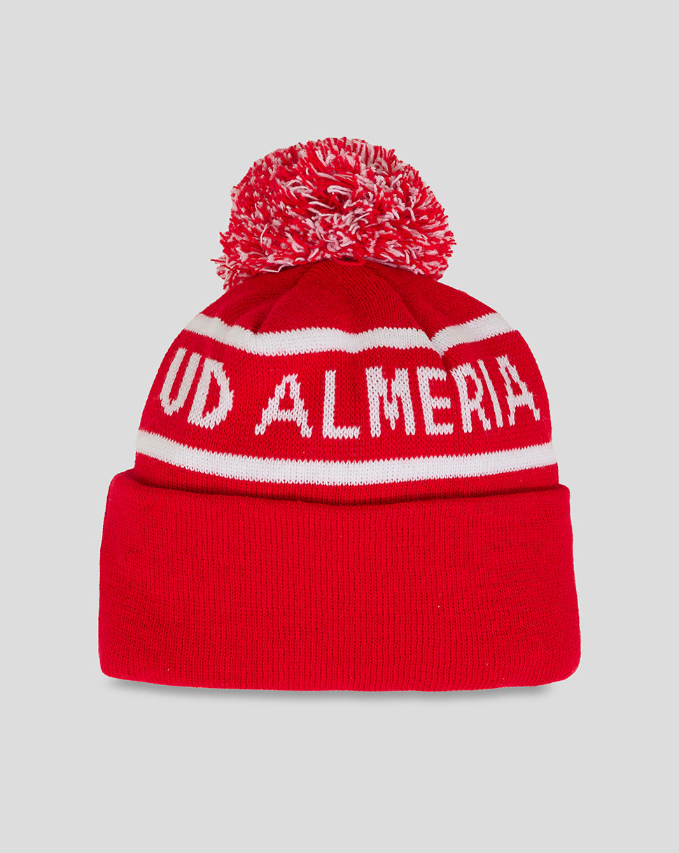 Side view of red Almeria Junior bobble hat showing white ALMERIA lettering and crest on the folded cuff.