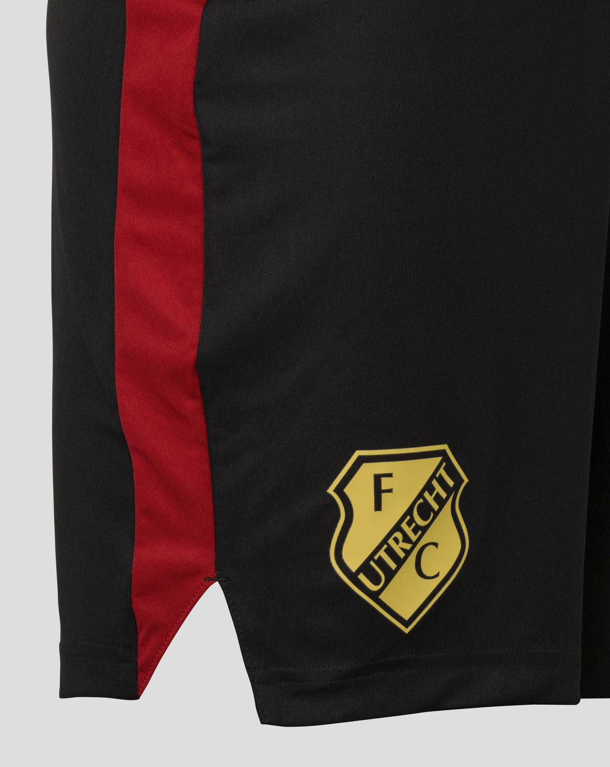 Detail of FC Utrecht training shorts showing black fabric with a red side stripe and gold crest at the hem