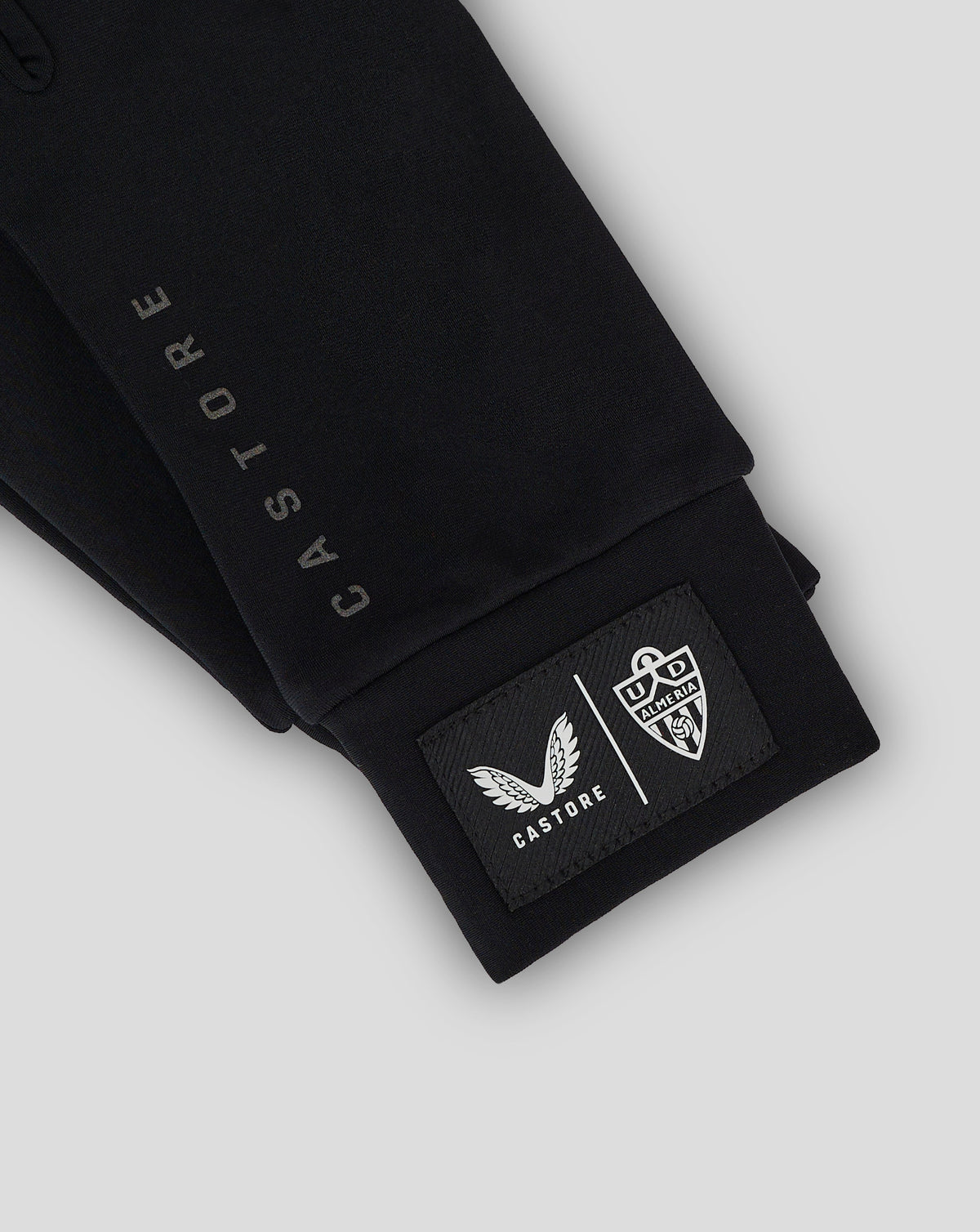 Close-up of black Almeria Club gloves with a crest patch and Castore badge