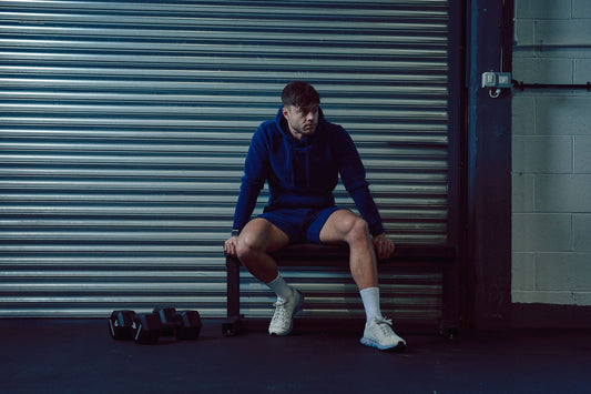 Athlete in a blue hoodie sits on a bench inside a gym with a metal shutter behind him