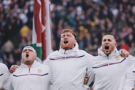 England rugby players in white jackets celebrate with arms around each other on the field.
