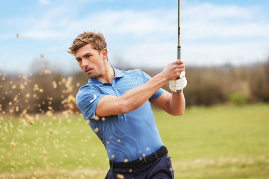 Golfer in a light blue polo swings a golf club on a sunny green course.