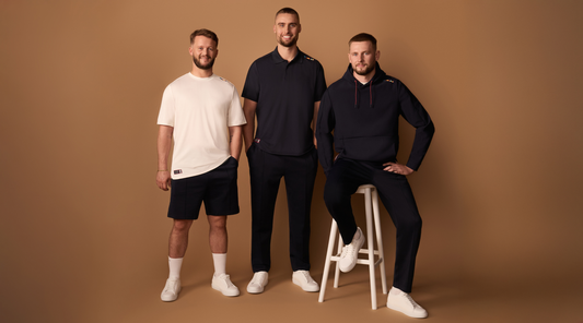 Three men pose in casual travel style outfits against a warm brown backdrop.