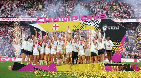 England Women's rugby team lifts a trophy on the pitch amid confetti and a champions banner with cheering crowd