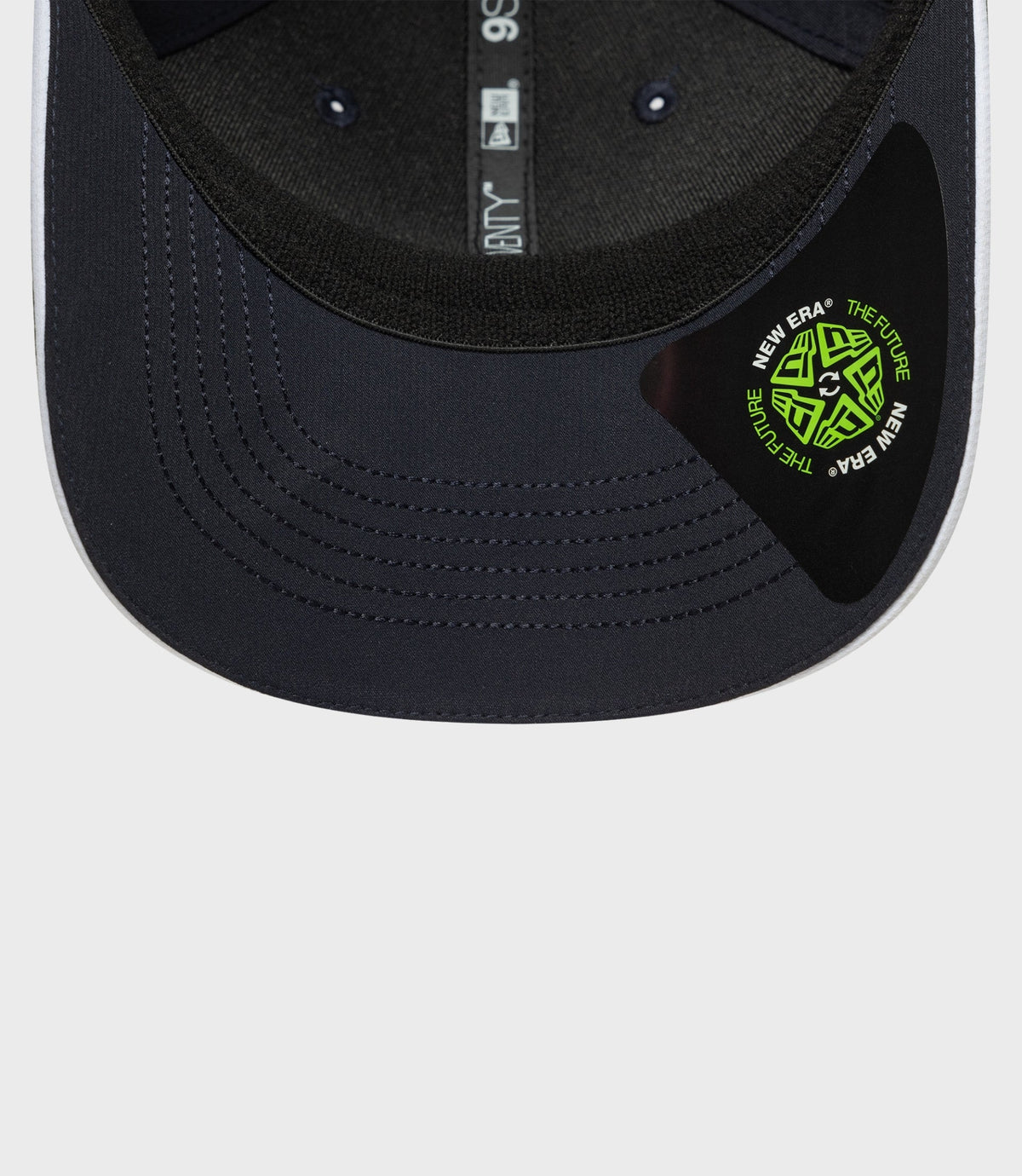 Close up of navy cap brim with neon green sticker and interior adjustable strap visible