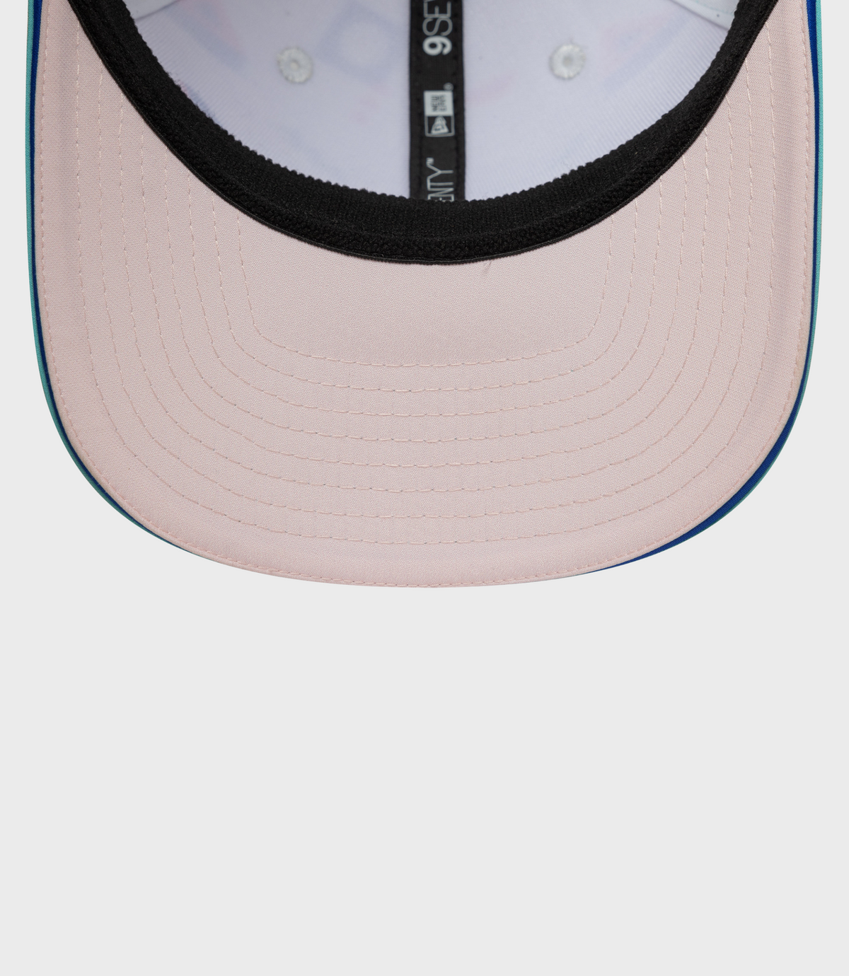 Close-up of pale pink crown with black inner trim and teal brim edge on a curved snap cap