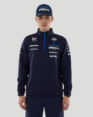 Person wearing a navy tracksuit with various sponsor logos on a gray background