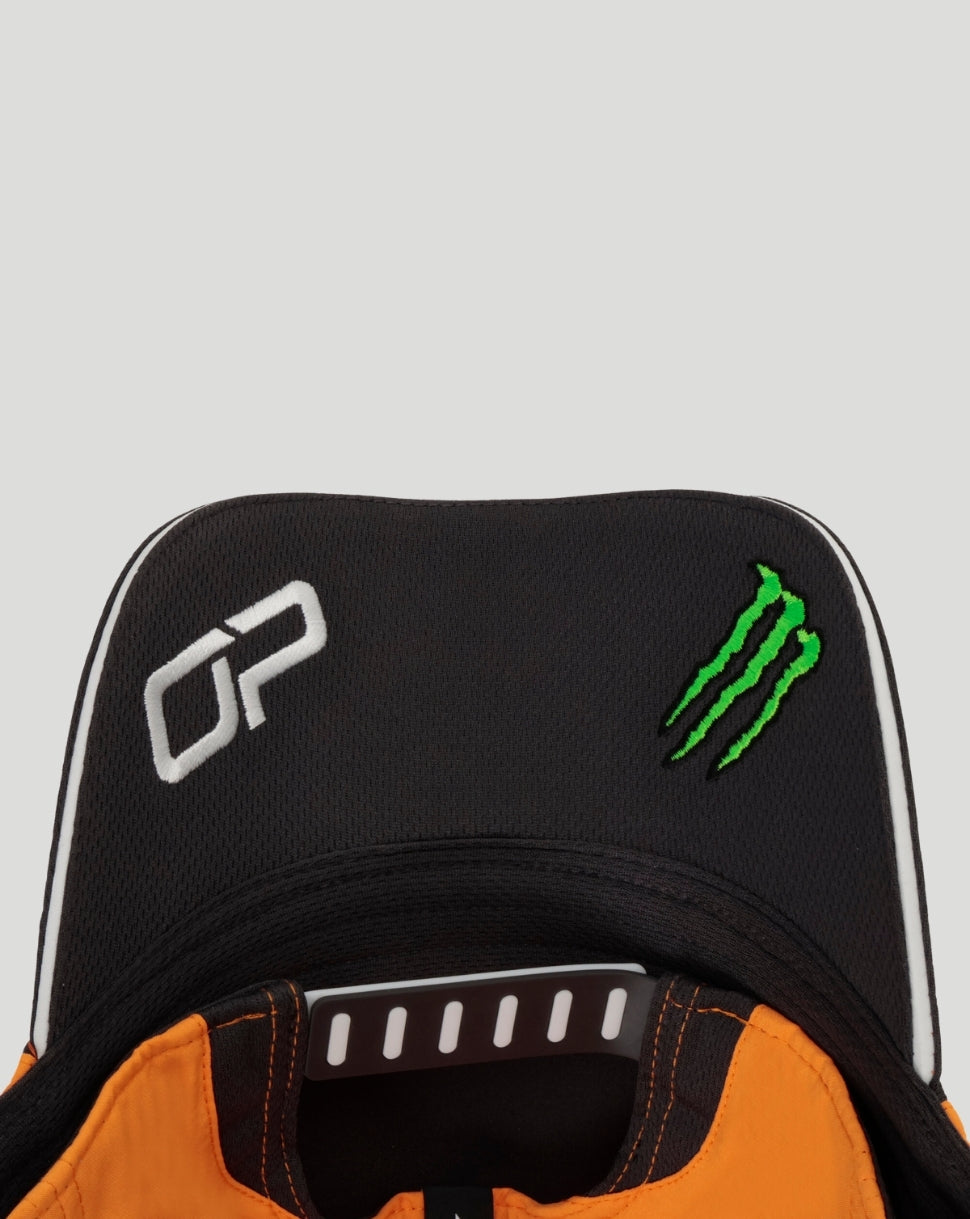 Close up of black Papaya McLaren cap with white Oscar Piastri initials and green Monster energy logo.
