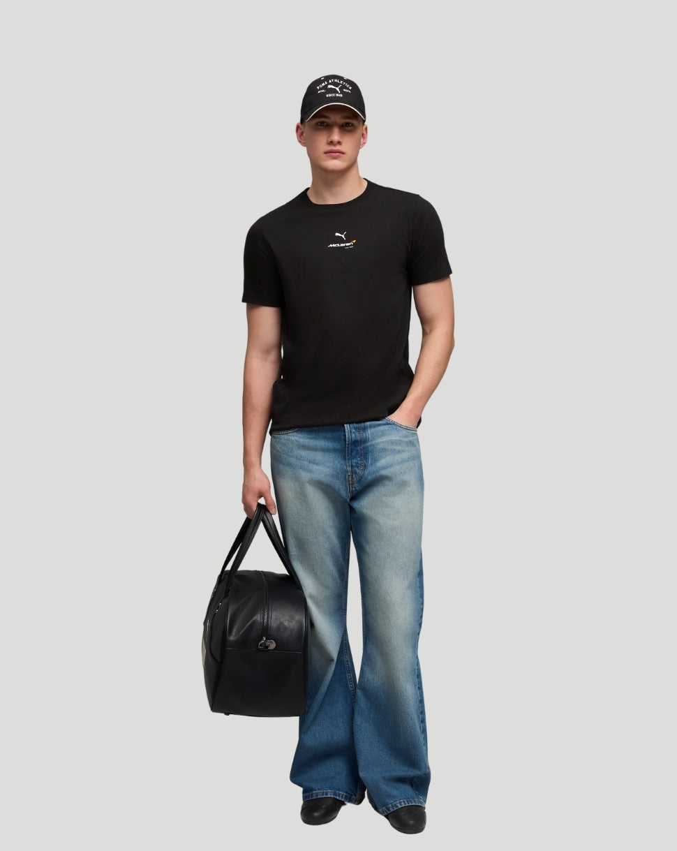 Male model wearing black McLaren T shirt with a small chest logo, jeans and a black duffel bag