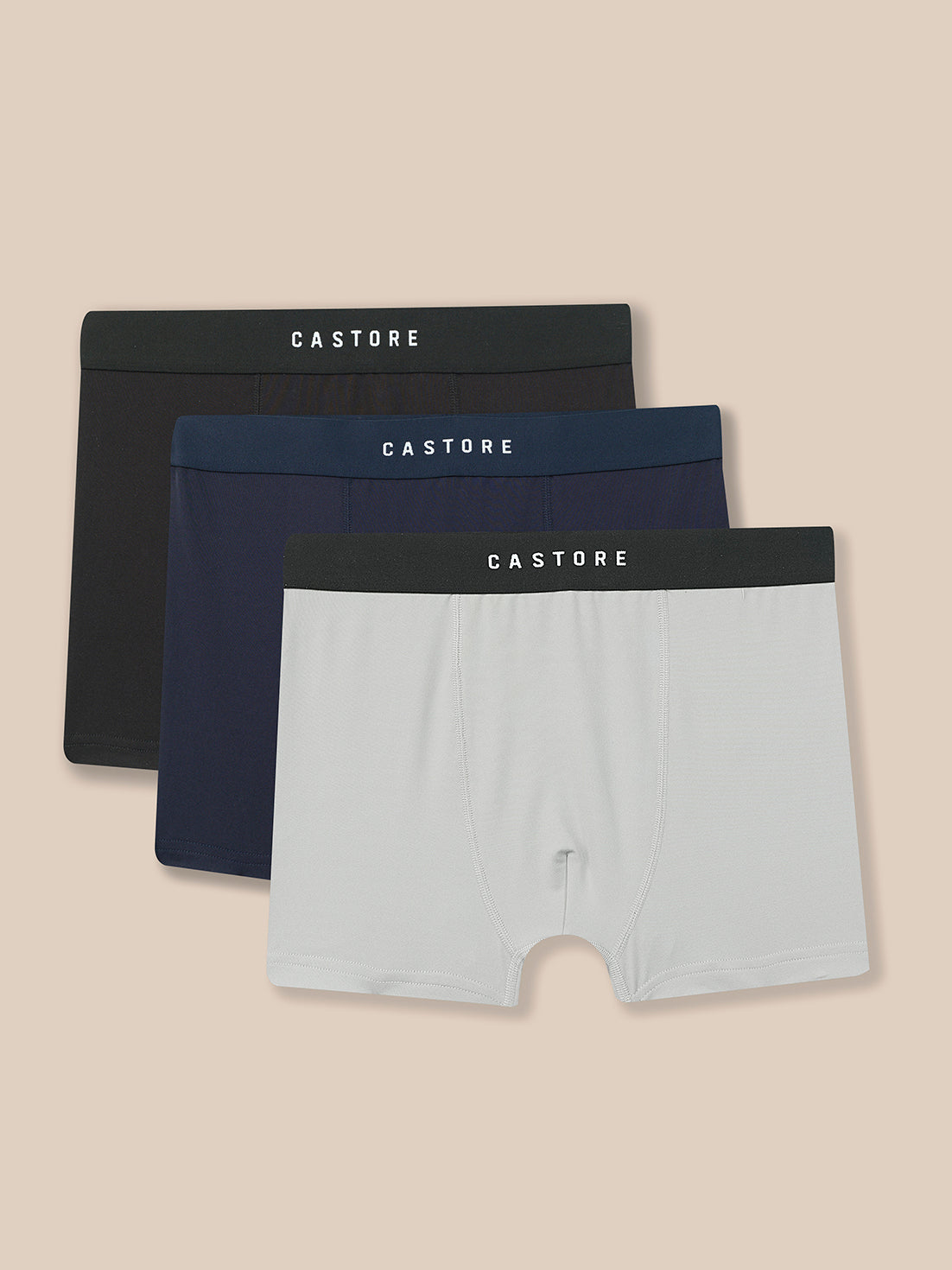Three pairs of Castore men's boxer briefs in black, navy blue, and light gray, arranged in a stacked fan layout against a solid beige background.
