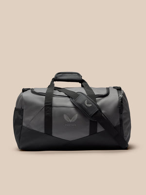 Core Holdall in gunmetal gray and black with padded grab handle, detachable shoulder strap, and a silver wing logo on the front.