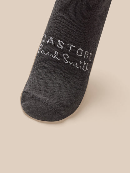 Dark gray sock with 'Castore Paul Smith' branding on a beige background