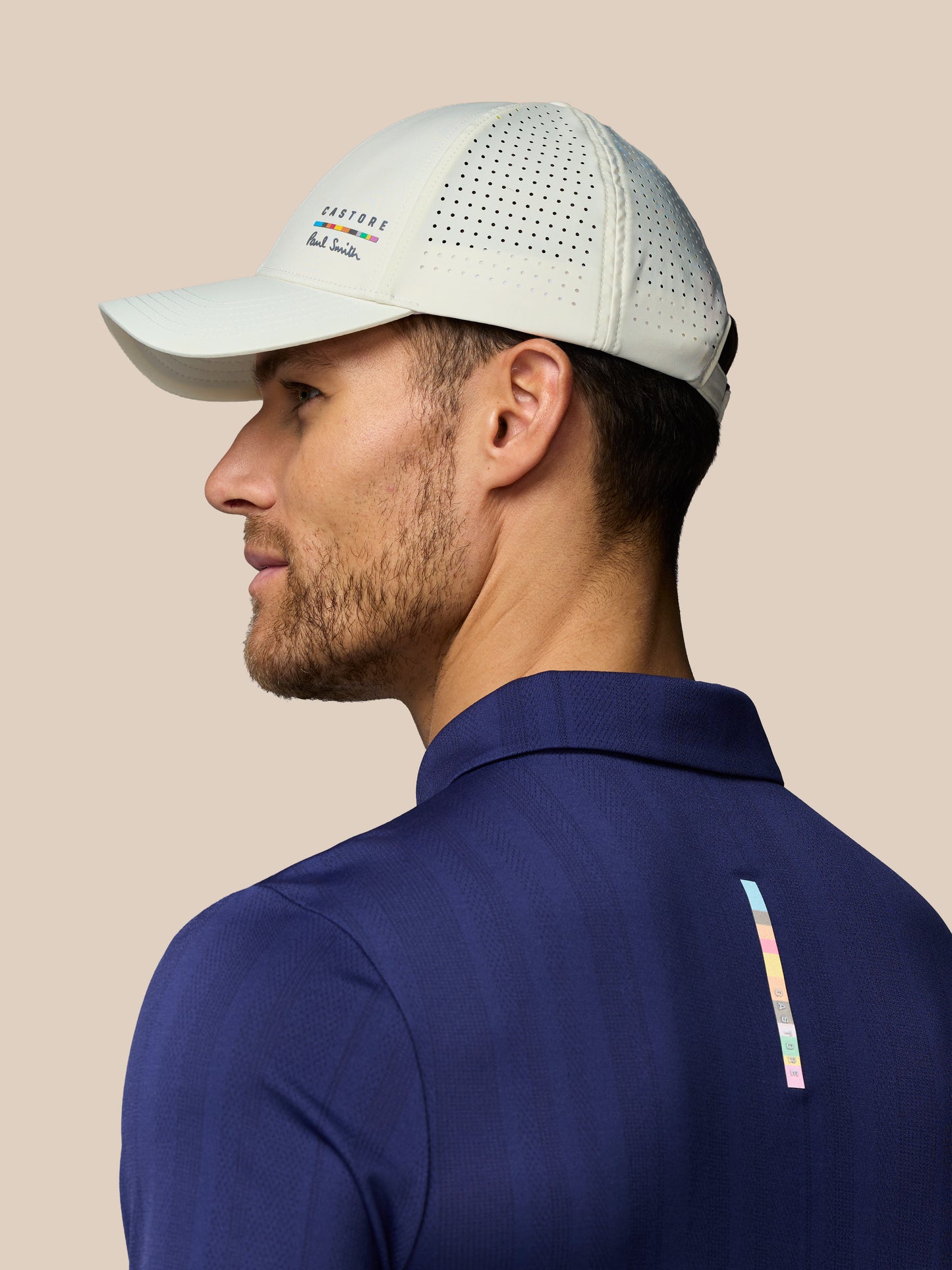 Man wearing a light gray cap and blue polo shirt with a brand logo on a beige background