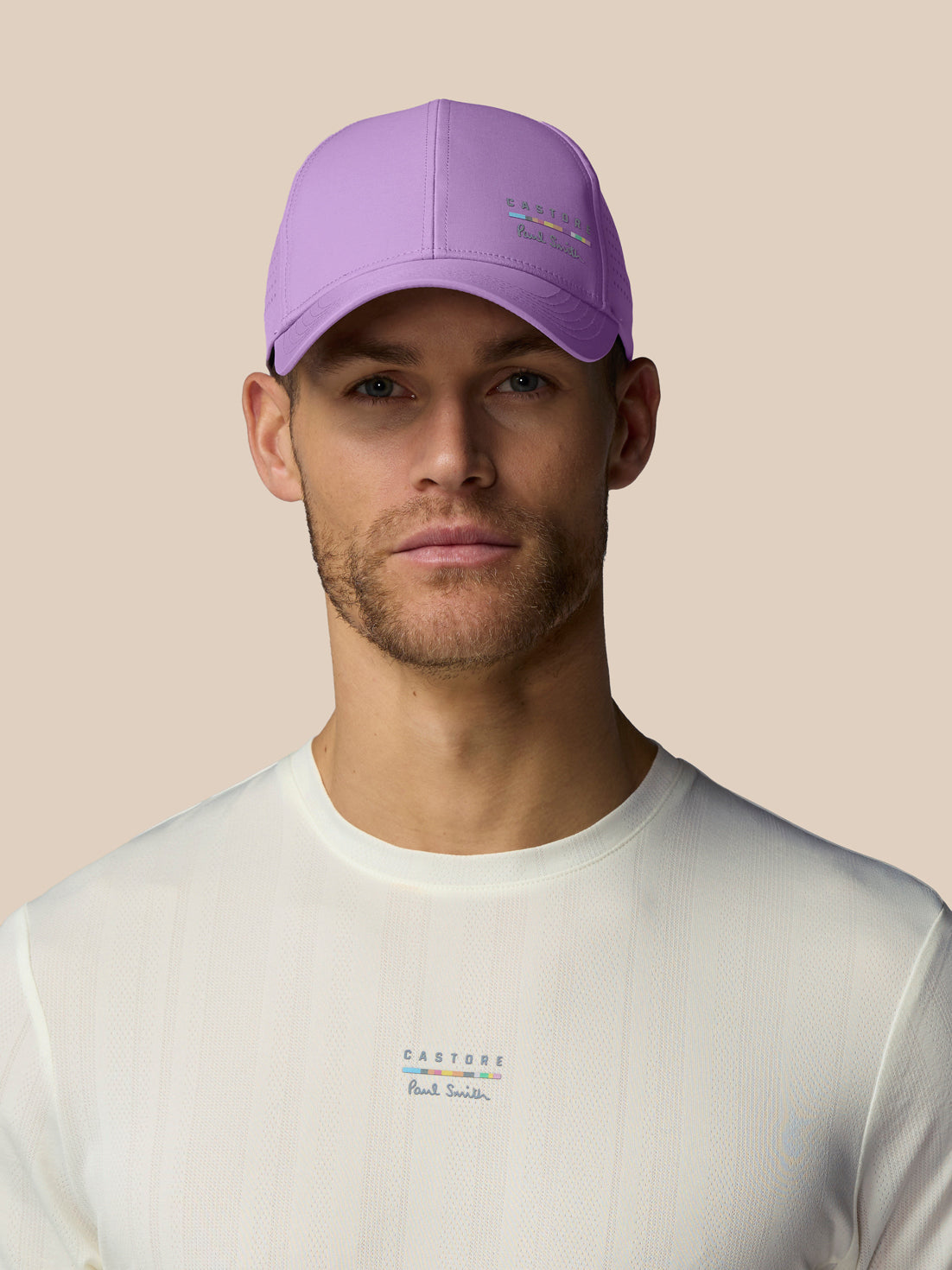 Man wearing a purple cap and white shirt with brand logos on a beige background