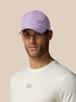 Man wearing a light purple cap and white shirt with brand logos on a beige background