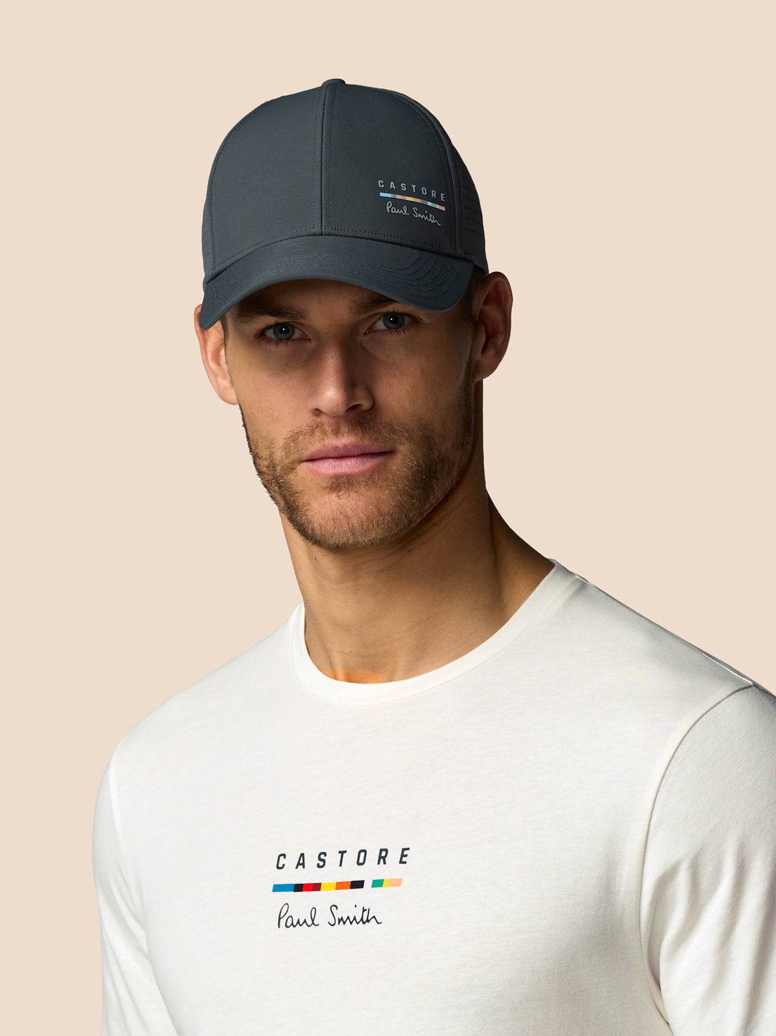 Man wearing a dark gray cap and white t-shirt with 'Castore' branding on a beige background