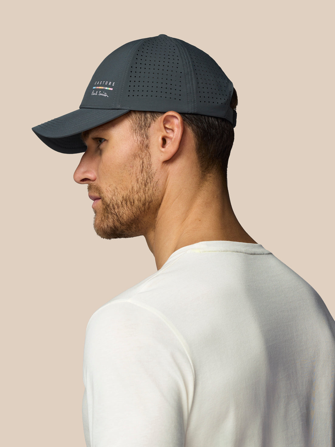Man wearing a dark grey cap with a visible brand logo on a beige background