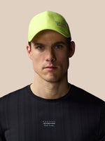 Man wearing a bright yellow cap and black t-shirt with branding on a beige background