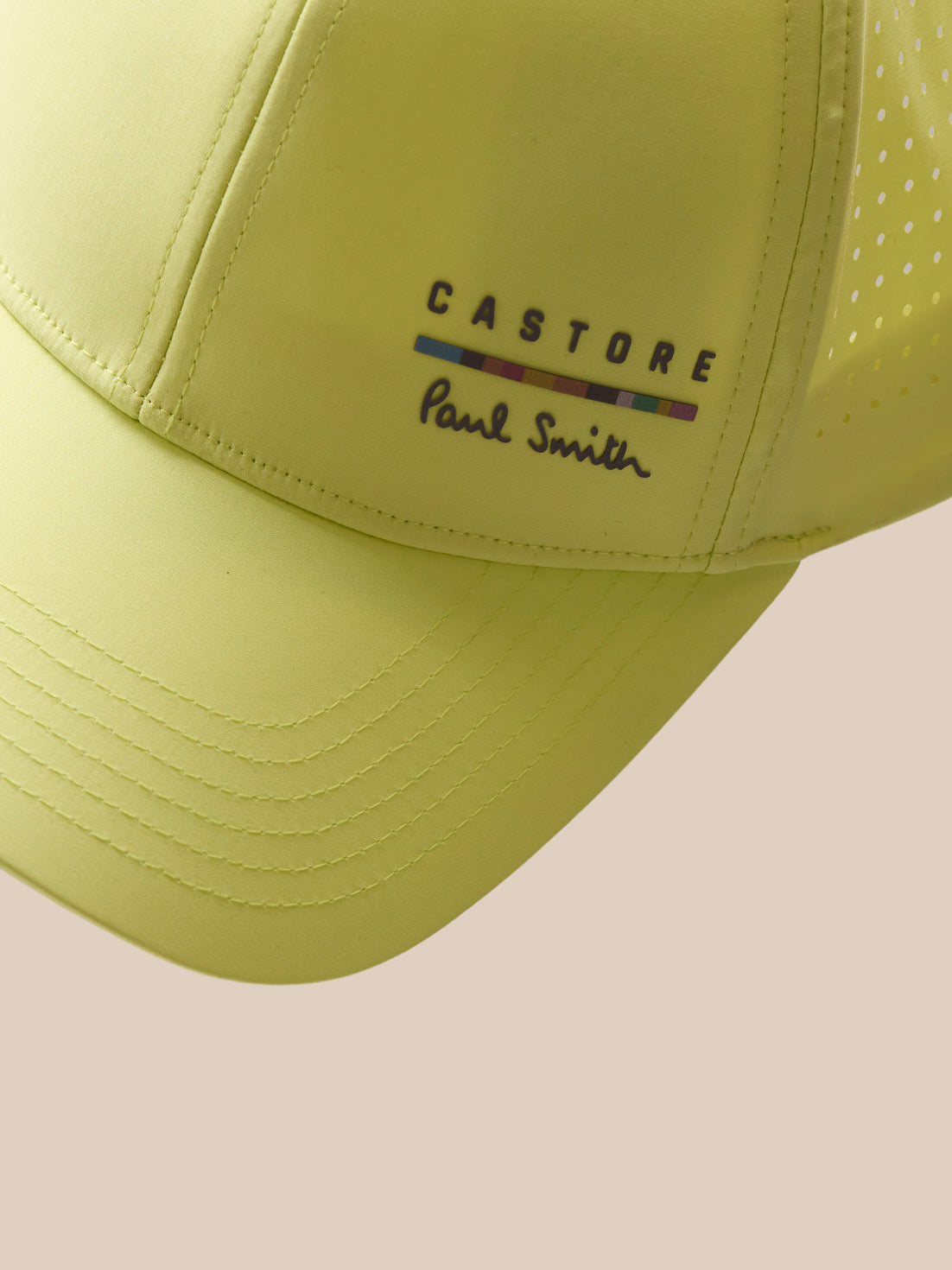 Yellow cap with 'Castore' and 'Paul Smith' logos on a beige background