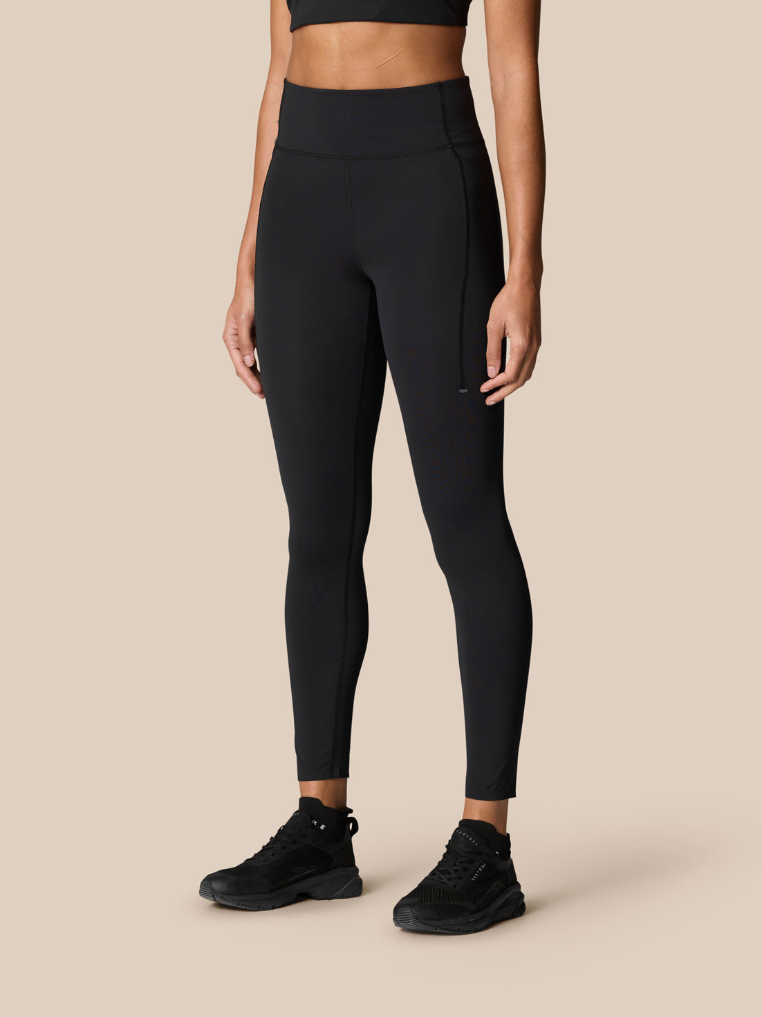 Front view of a model wearing black Zone full length training leggings with mid rise and left leg Castore logo