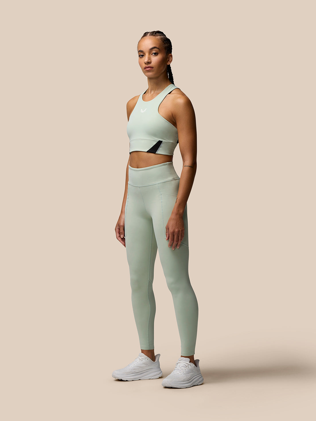 Female model wearing Sage Apex training leggings and matching sports bra in a studio setting.