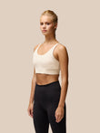 Model wearing beige Flow Training Sports Bra with cropped silhouette and black leggings