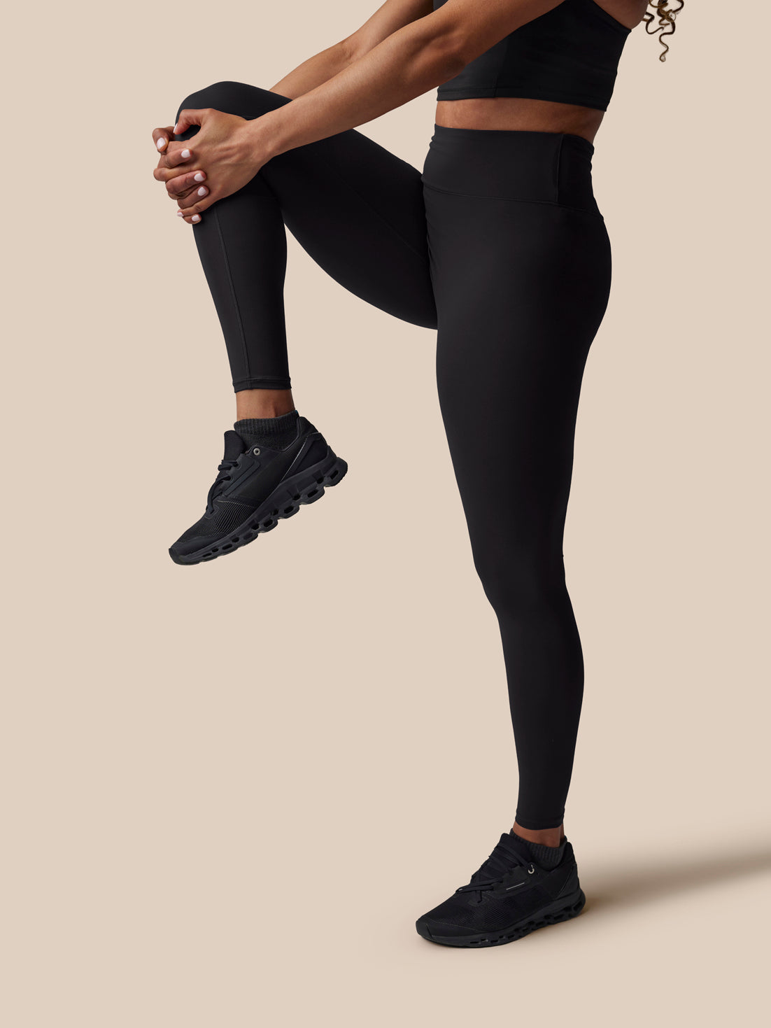 Person wearing black athletic leggings and shoes on a beige background