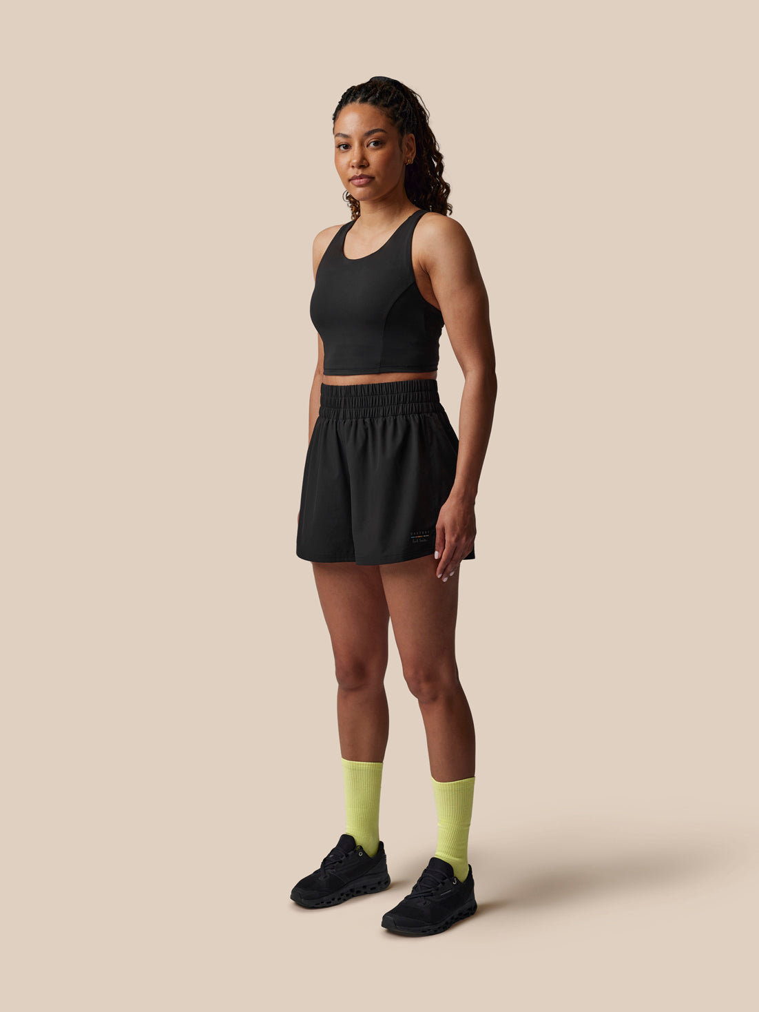 Woman wearing a black athletic outfit with yellow socks on a beige background
