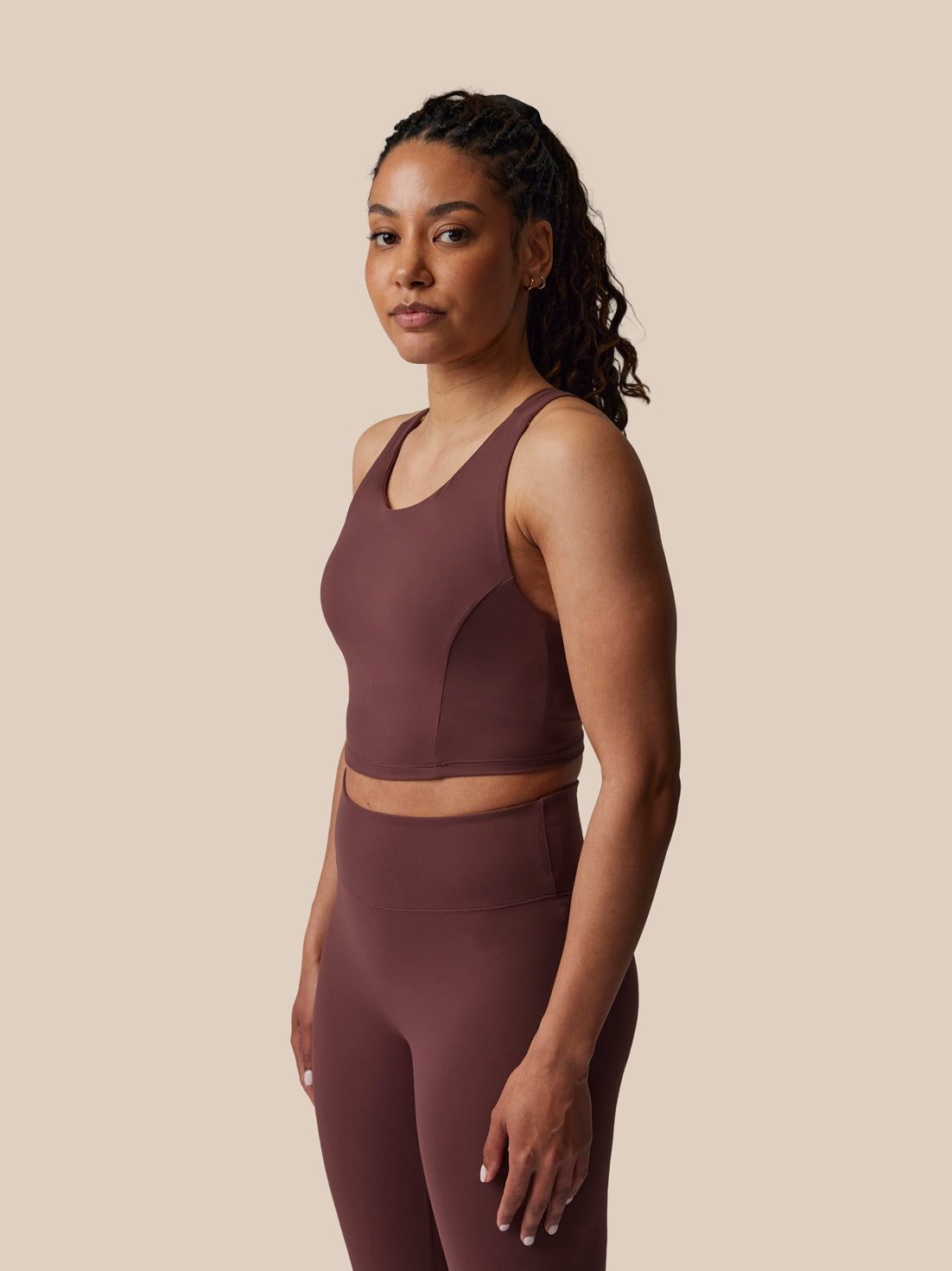 Woman wearing a brown sports bra and leggings set against a beige background