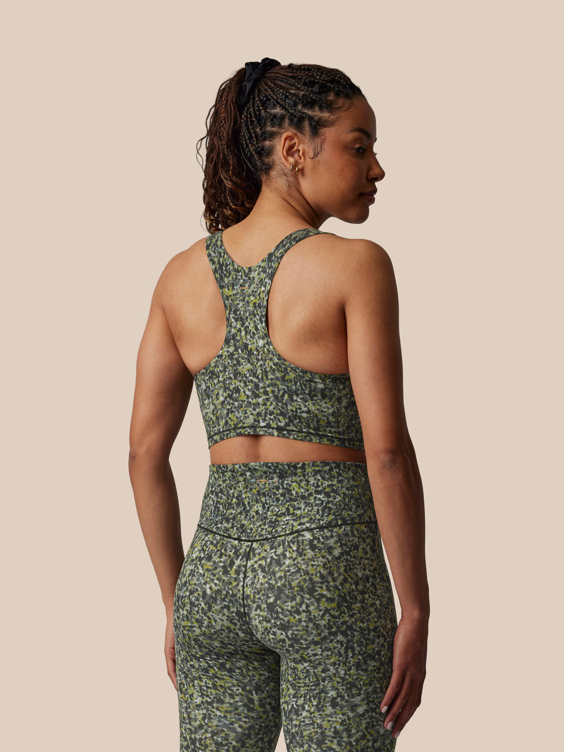 Woman wearing a green floral sports bra and leggings set on a beige background