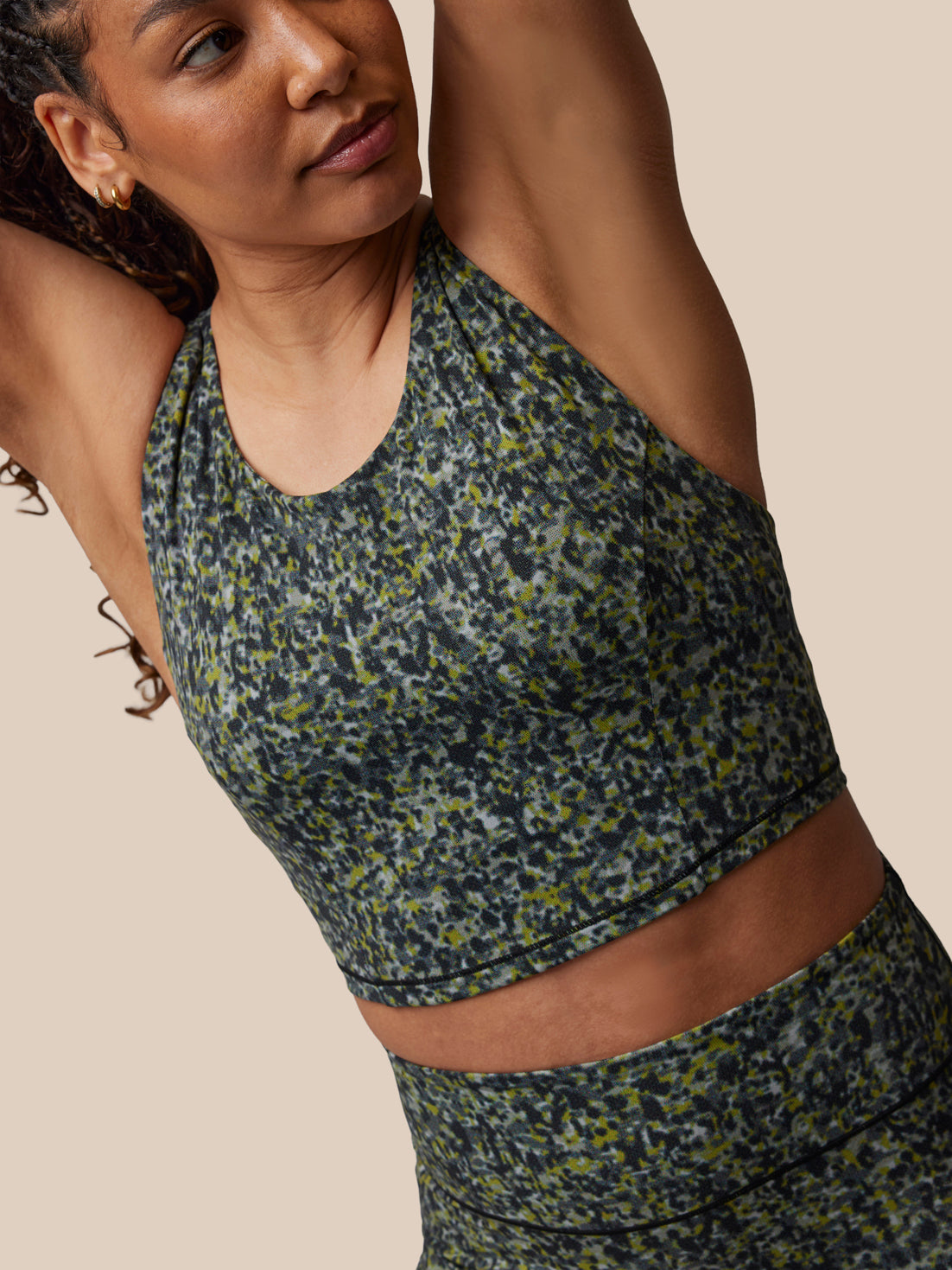 Woman wearing a green and black patterned sports bra and leggings on a beige background