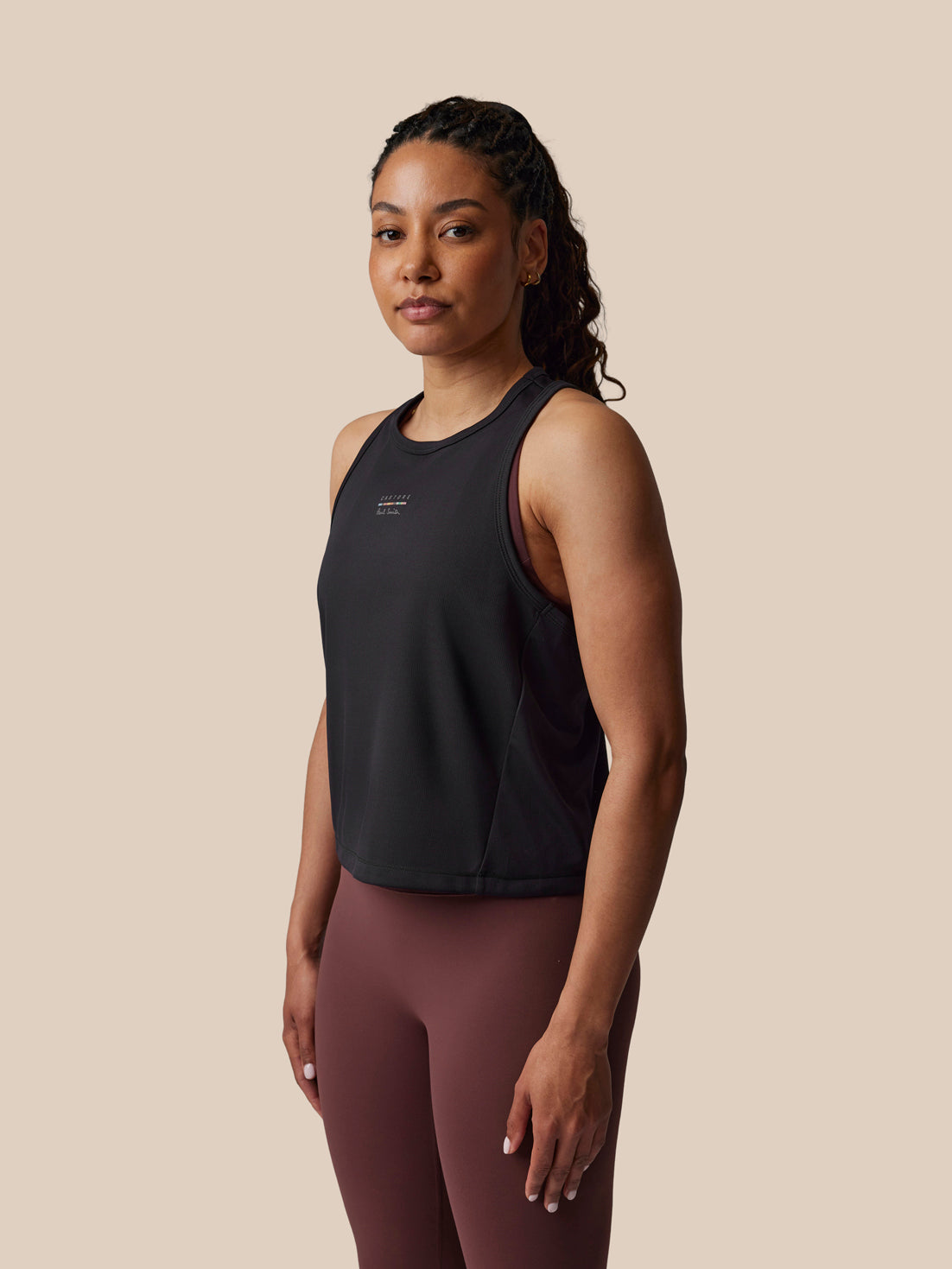 Woman wearing a black sleeveless top and maroon leggings on a beige background