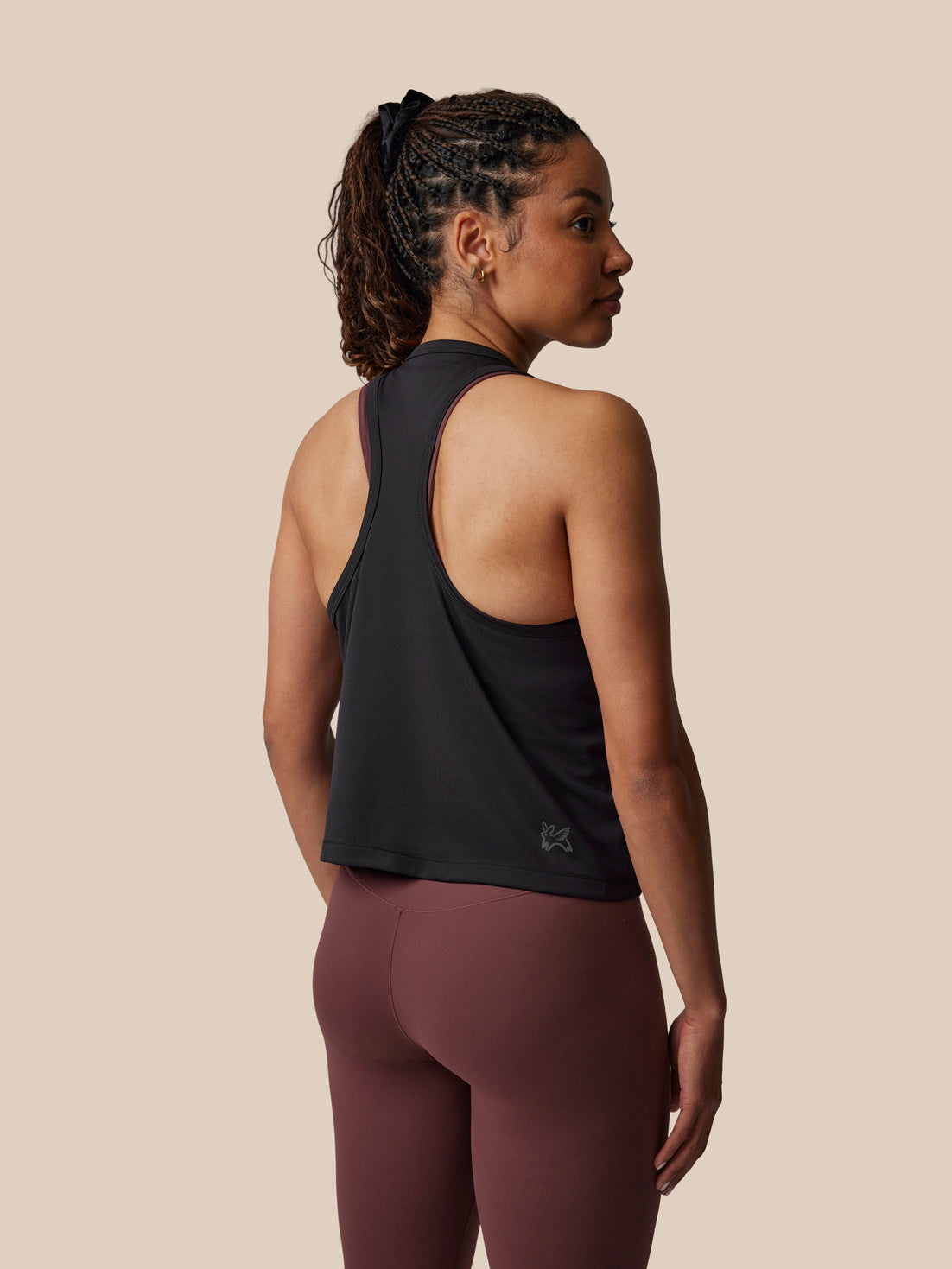 Woman wearing a black tank top and maroon leggings on a beige background