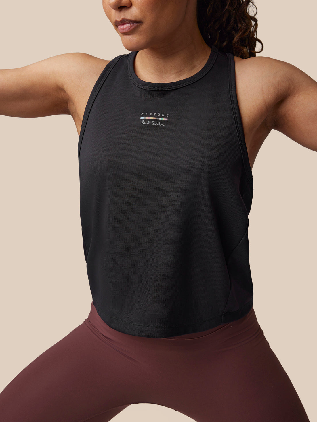 Person wearing a black athletic tank top with a brand logo on a beige background